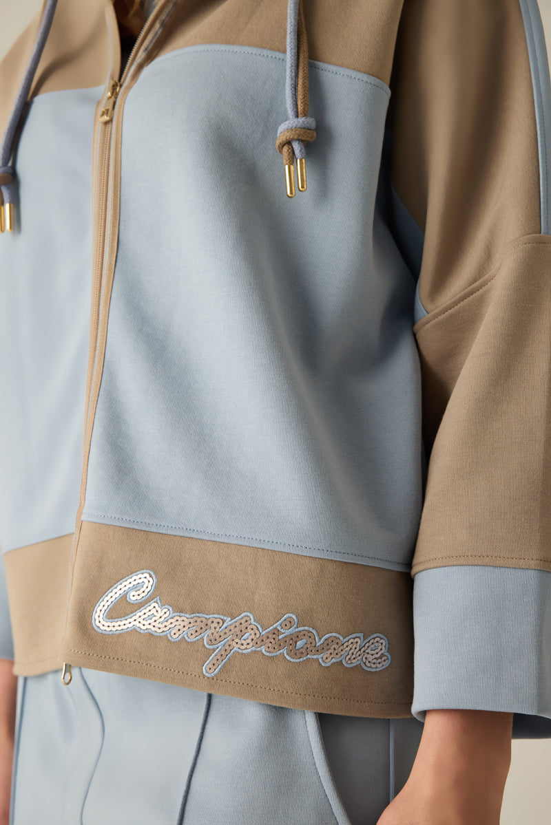 Hochwertige Damen-Sweatshirtjacke mit Kapuze und Doppel-Kordel, modernem Materialmix in Caramel & Blau und überschnittenen Schultern. Der verlängerte Rücken sorgt für eine lässige Silhouette, während die Pailletten-Stickerei am Saum edle Akzente setzt...